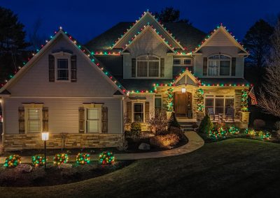 red, white, and green lights on a home bushes and garland in rexford ny